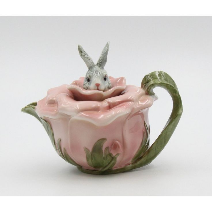 a ceramic teapot with a rabbit in it's mouth sitting on top of a pink flower