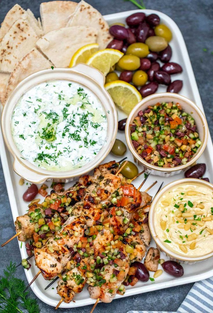 a platter filled with grilled chicken, olives, pita bread and other appetizers