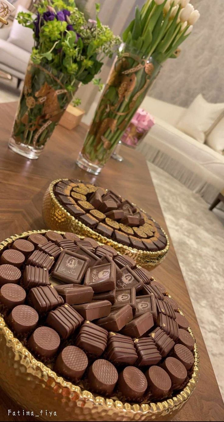 two chocolate cakes sitting on top of a table next to vases filled with flowers