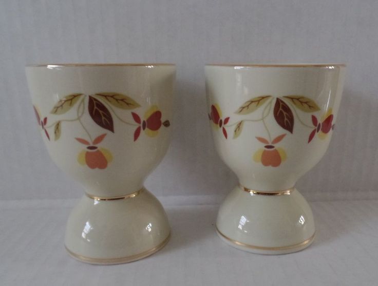 two white vases with red and yellow leaves on them sitting next to each other