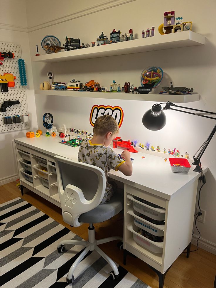 a young boy sitting at a desk with legos on the shelves and toys in front of him