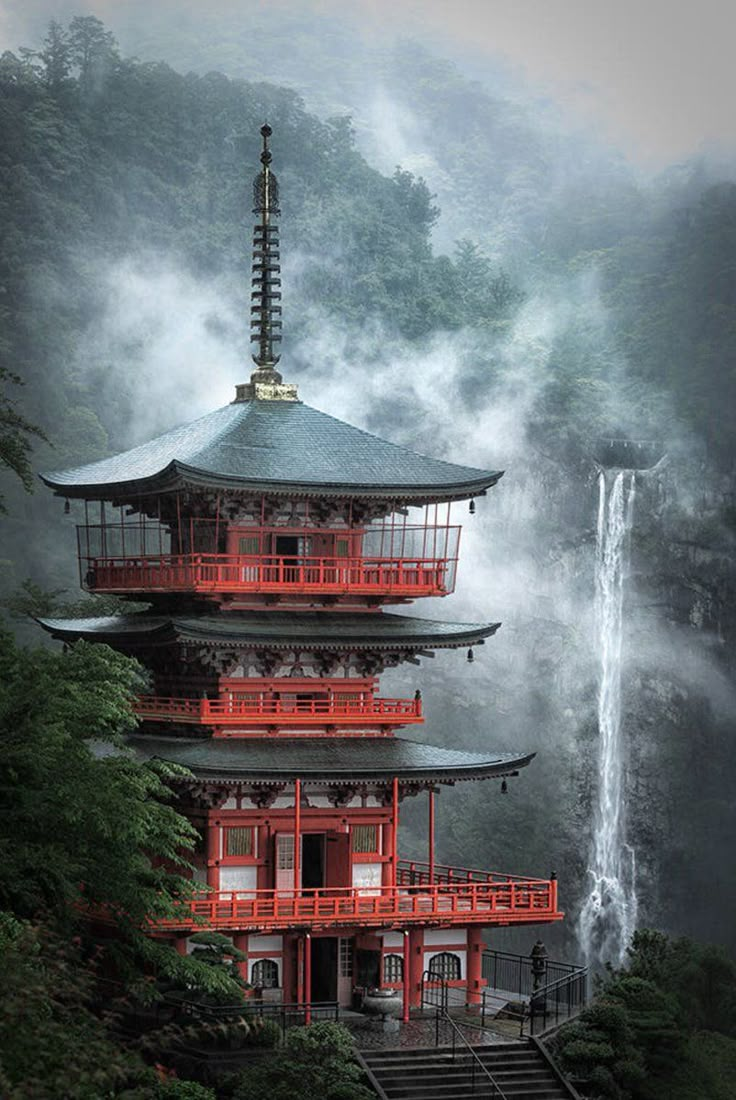 a tall pagoda with a waterfall in the background and foggy sky above it, surrounded by trees