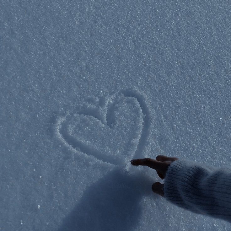 a person's hand is touching the snow with a heart drawn in it