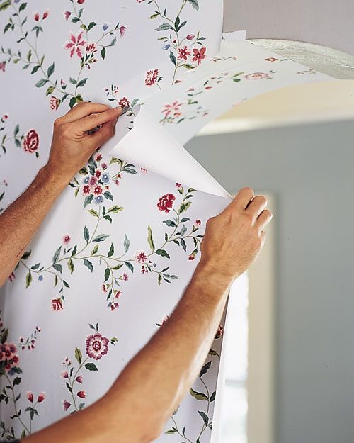 a man working on a floral wallpaper with white paper and red flowers in the background