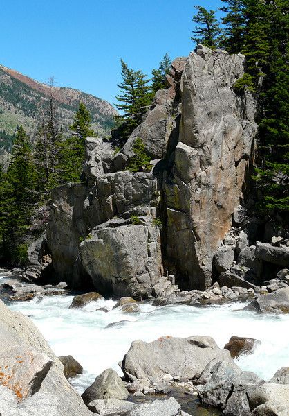 a man standing on top of a large rock next to a white water rushing river