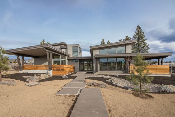 a modern house in the middle of a dirt lot with trees and rocks around it