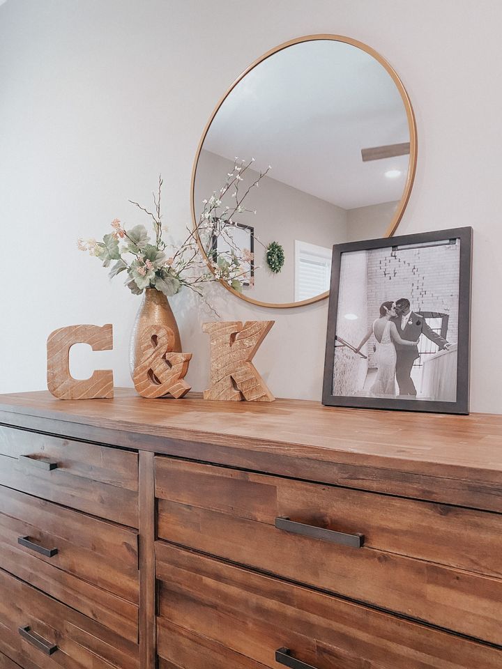 a wooden dresser topped with a mirror next to a vase filled with flowers and letters