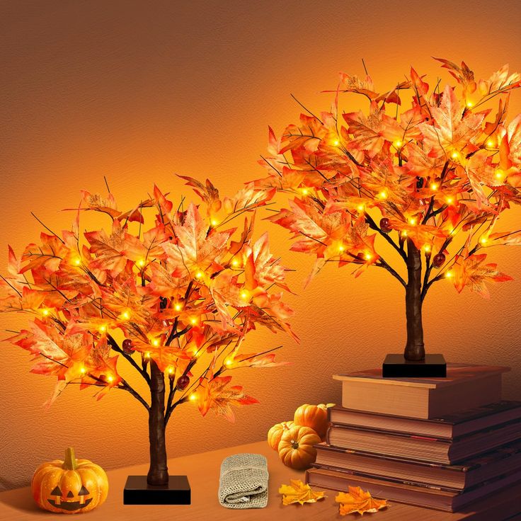 two lighted trees with pumpkins and books on a table