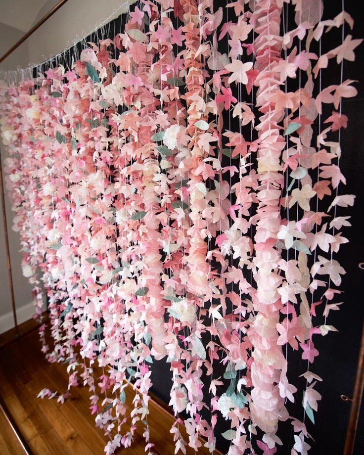 pink and white paper flowers hanging from strings on the wall in front of a staircase