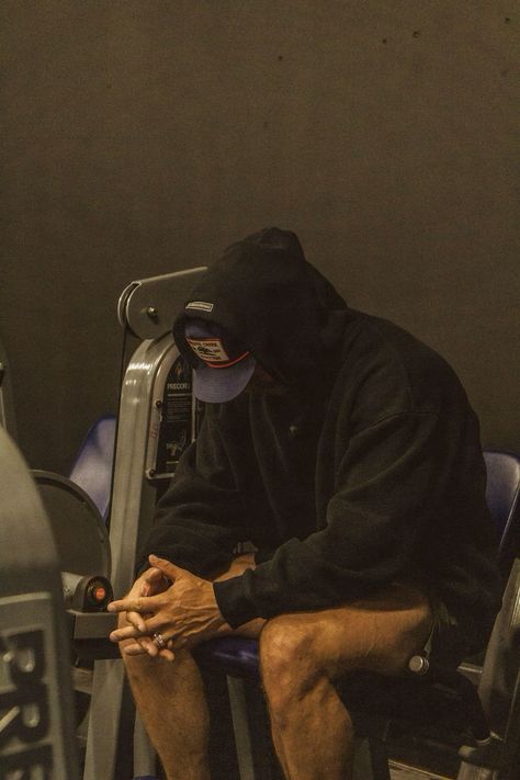 a man sitting on top of a gym machine with his hands in his pockets and wearing a black hoodie