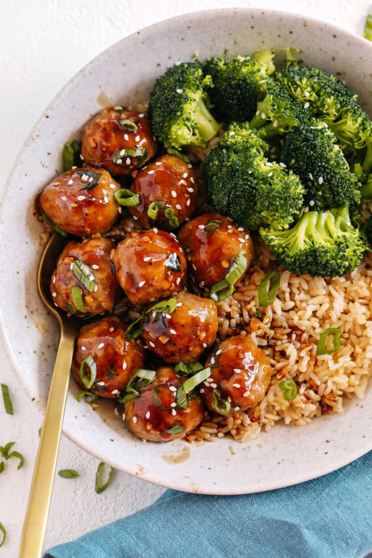 a white bowl filled with meatballs and broccoli on top of brown rice