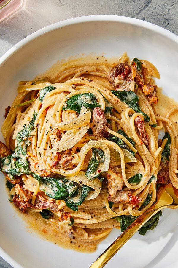 a white bowl filled with pasta and spinach on top of a marble countertop