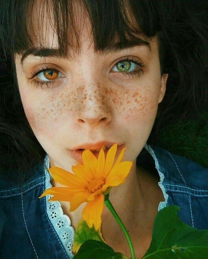 a woman with freckles on her face holding a flower