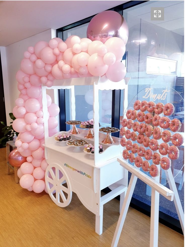 a doughnut cart with pink balloons and donuts on the table for desserts