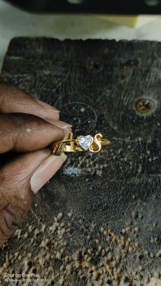 a hand holding a gold and diamond ring on top of a piece of wood with holes in it