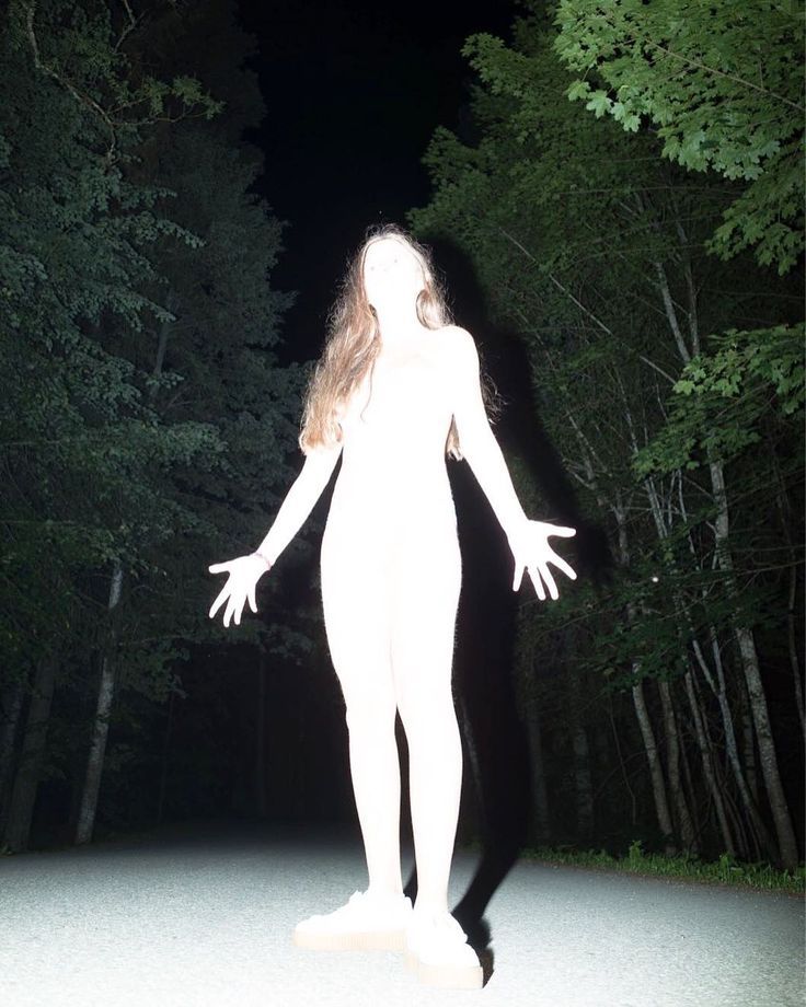 a woman standing in the middle of a forest at night with her arms outstretched out