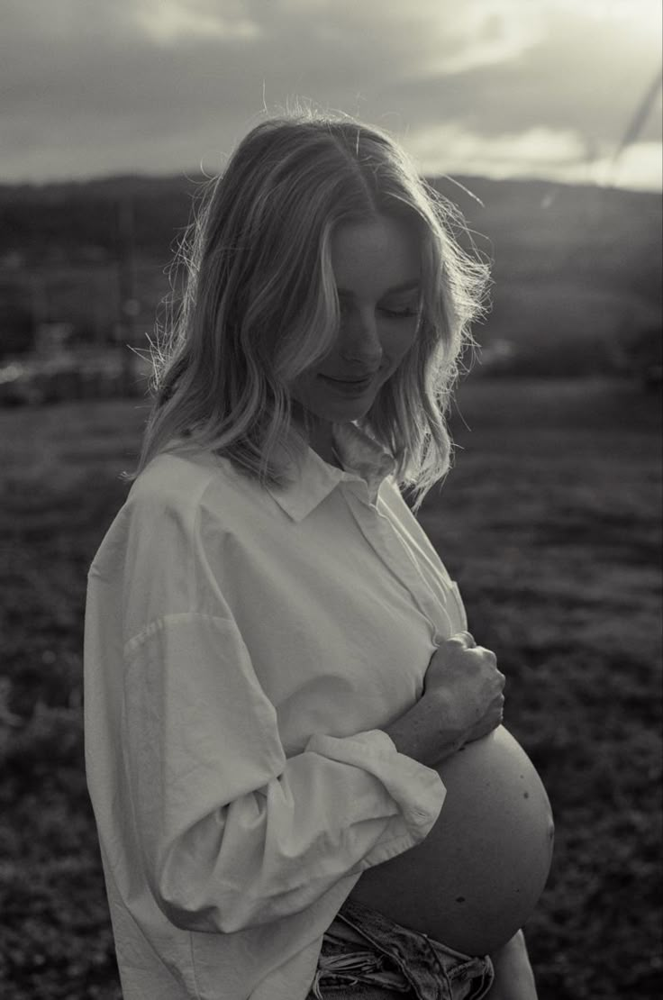 a pregnant woman standing in a field with her hands on her stomach and looking down