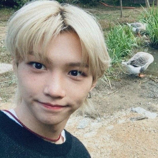 a young boy with blonde hair standing in front of a pond and birds on the ground