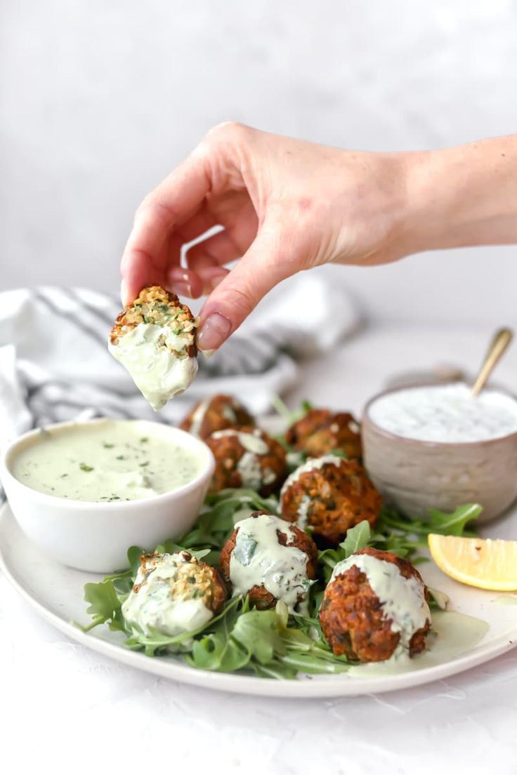 a person dipping some food on top of a white plate with salad and dips