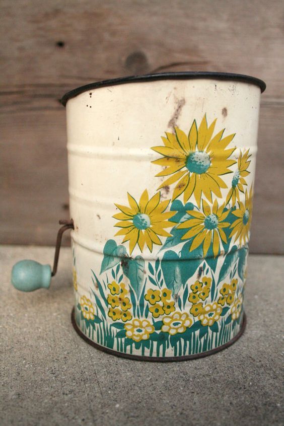 an old tin can with yellow flowers painted on it sitting next to a wooden wall