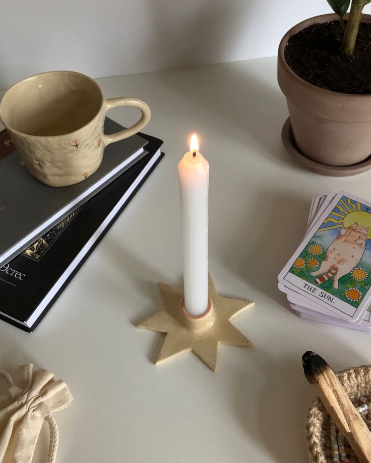 a lit candle sitting on top of a table next to some cards and a potted plant