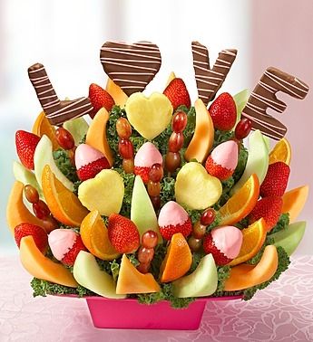 a pink bowl filled with assorted fruit and chocolate covered candies in the shape of hearts