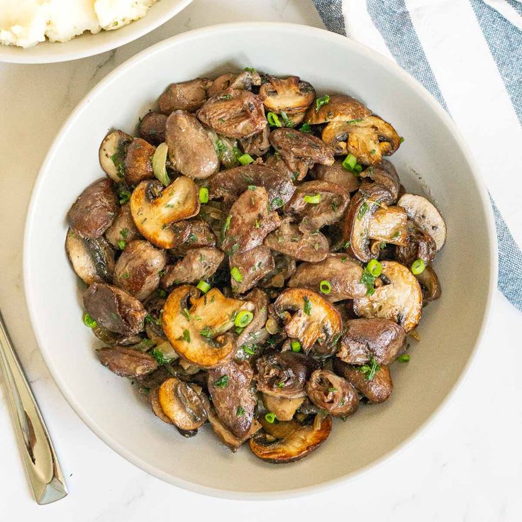 a white bowl filled with mushrooms and peas next to a plate of mashed potatoes