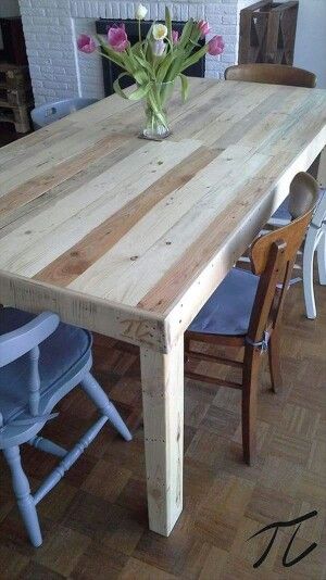 a wooden table sitting on top of a hard wood floor next to chairs and a vase with flowers in it