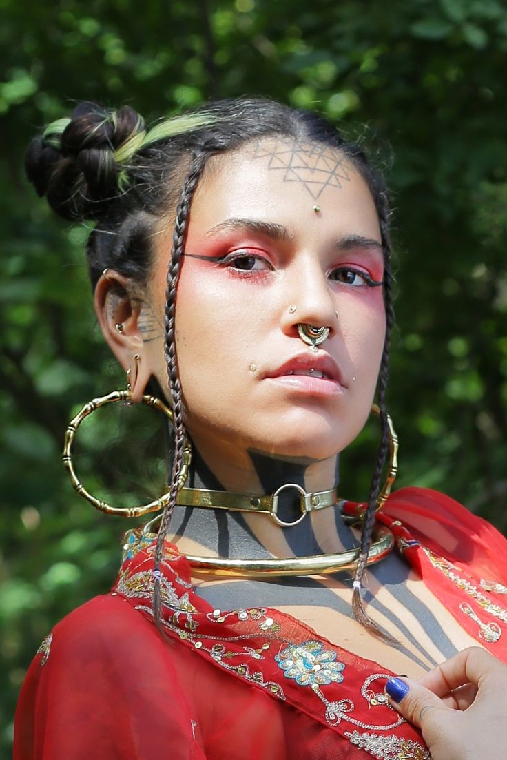 a woman with piercings on her nose and chest is wearing a red dress in front of some trees