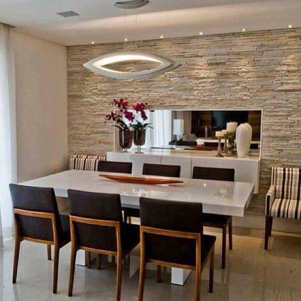 a dining room table with chairs and a vase on top of it in front of a stone wall