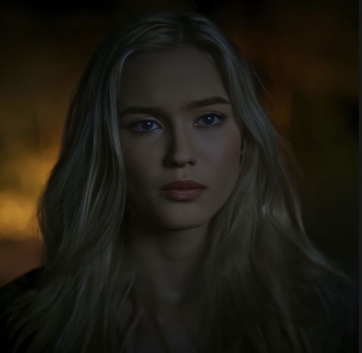 a woman with long blonde hair and blue eyes is looking at the camera while standing in front of a dark background