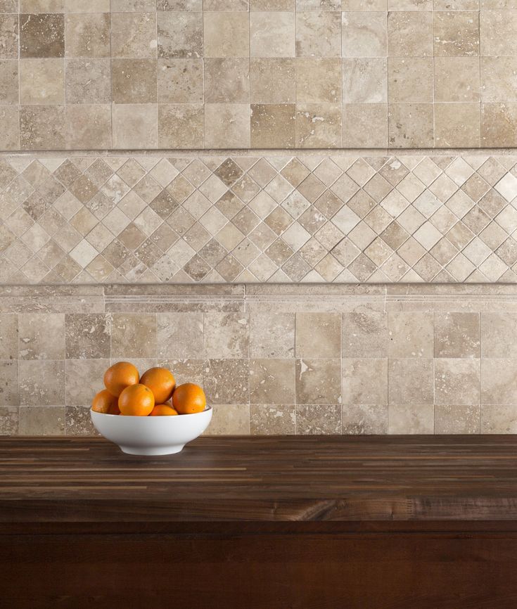 a bowl filled with oranges sitting on top of a wooden table next to a tiled wall