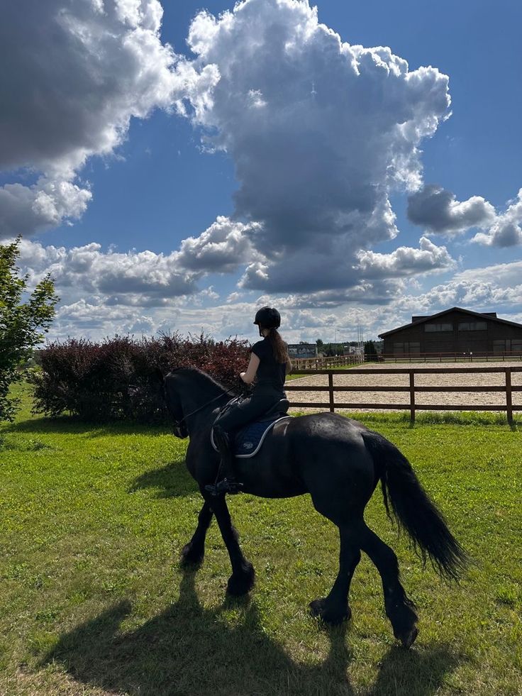 a woman riding on the back of a black horse across a lush green grass covered field