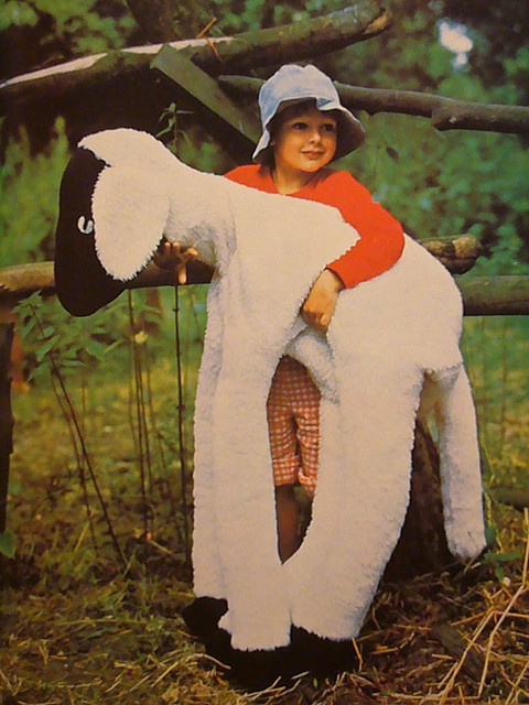 a young boy dressed in a sheep costume sitting on a tree stump with his legs spread out