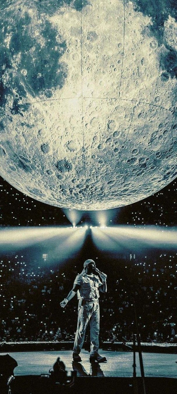 an astronaut standing on stage in front of a giant moon with his arms out to the side