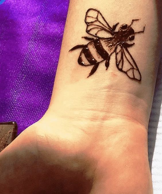 a small tattoo on the wrist of a woman with a bee on it's arm