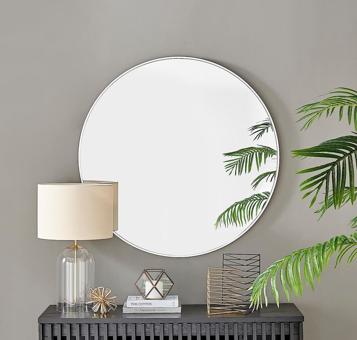 a round mirror sitting on top of a table next to a lamp and a potted plant