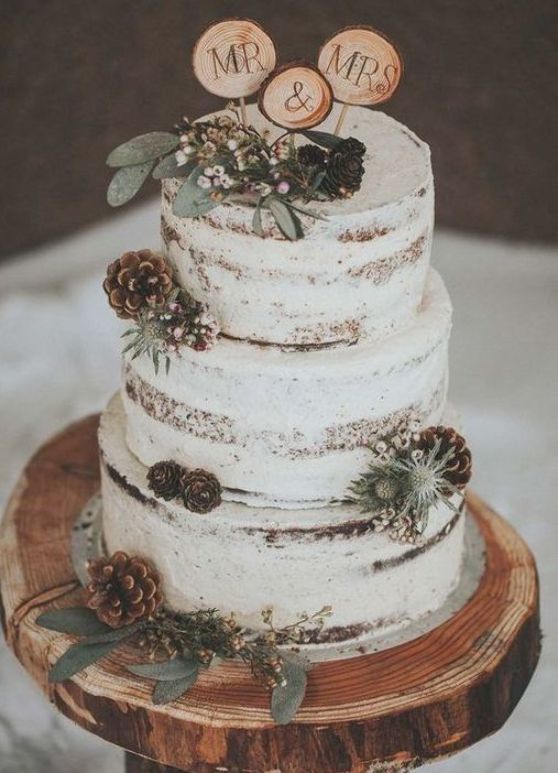 a three tiered cake with pine cones and greenery on top is sitting on a wooden stand