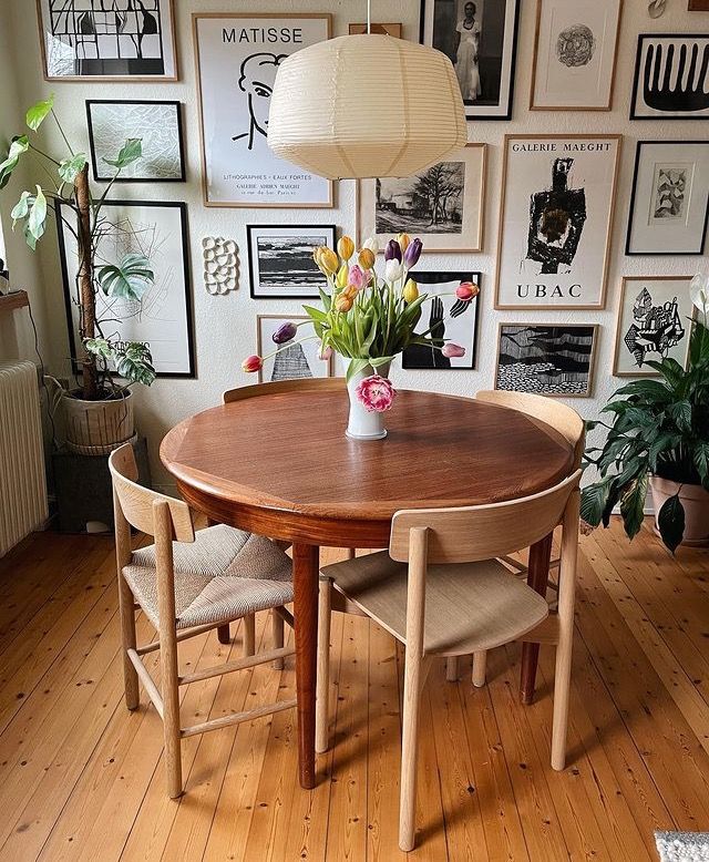 a dining room table and chairs in front of a wall with pictures on the walls