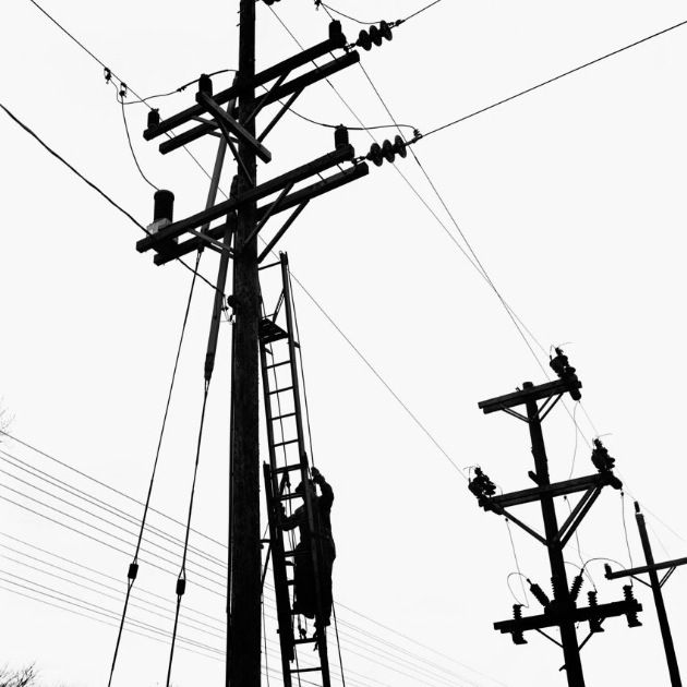 black and white photograph of people working on an electric pole with power lines in the background