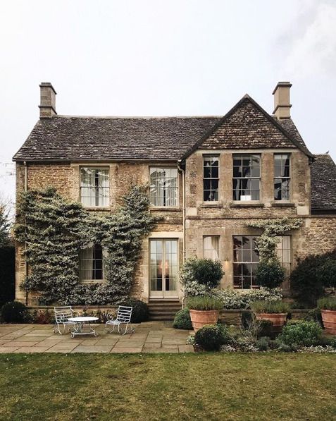 an old house with ivy growing on it's walls and two chairs in the front yard