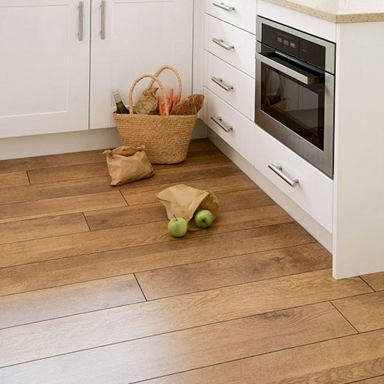 a kitchen with wooden floors and white cabinets, an oven, sink, and clock on the wall