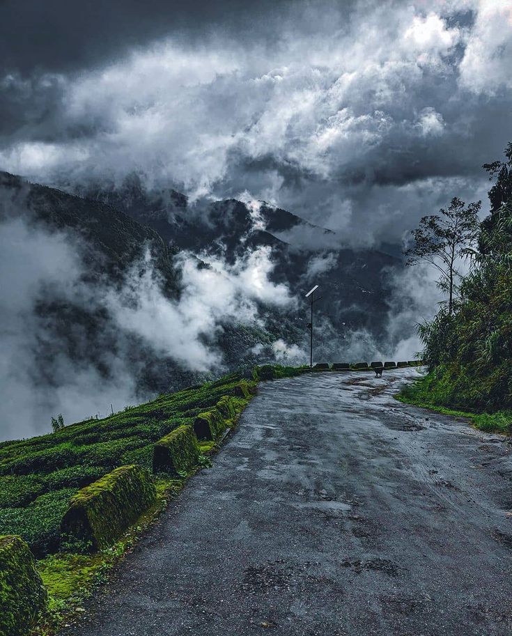 an empty road surrounded by lush green mountains under a cloudy sky in the middle of nowhere