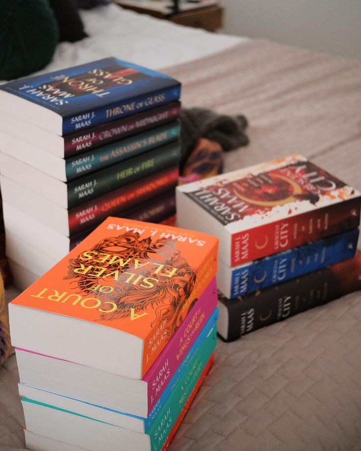 a stack of books sitting on top of a bed next to a pile of other books