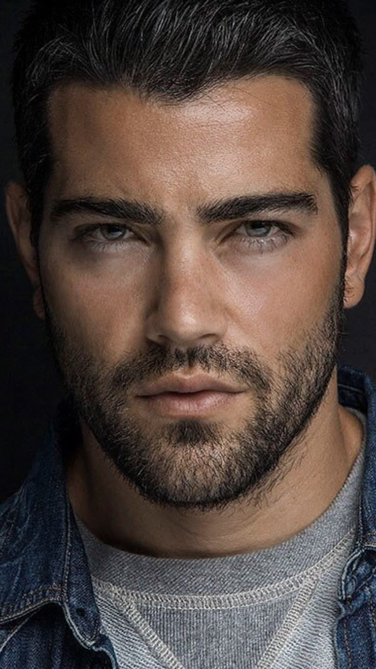 a close up of a man wearing a denim jacket and looking at the camera with a serious look on his face