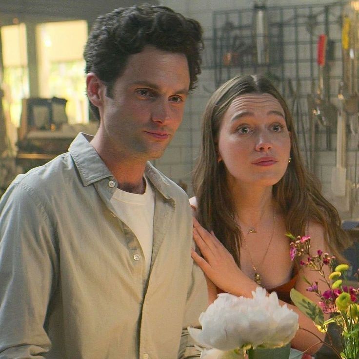 a man and woman standing next to each other in front of a vase with flowers