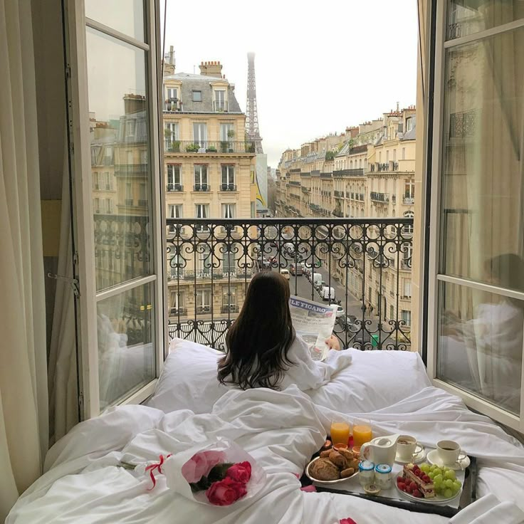 a woman sitting on top of a bed in front of a window with an open view