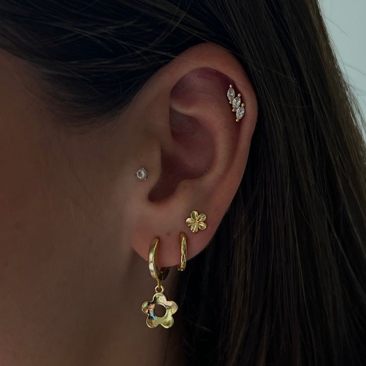 a close up of a woman's ear wearing gold earrings with flowers on them