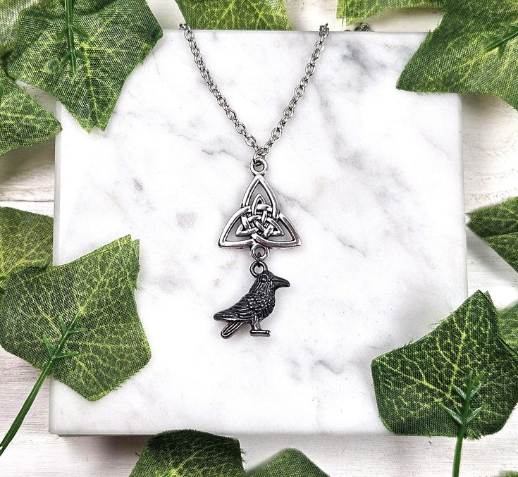 a necklace with a bird on it and a celtic knot in the shape of a triangle