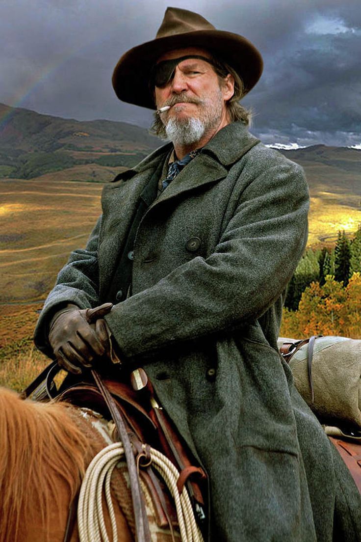 a man wearing a hat and coat sitting on a horse with a rainbow in the background